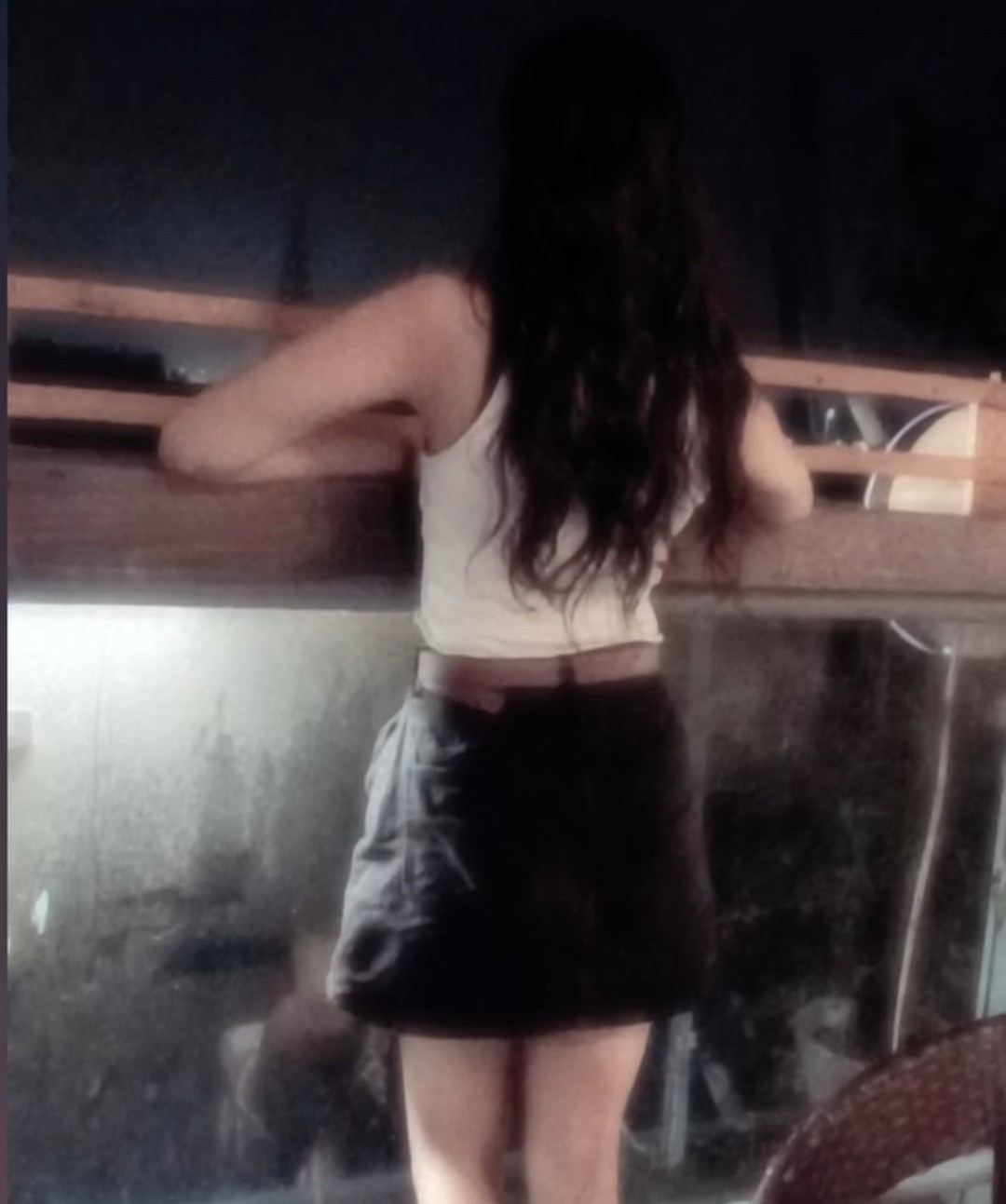 Tanya in a white top and black skirt, back turned, standing confidently indoors